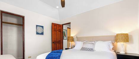 Quarto com cama, mesas de cabeceira, um banquinho e uma porta.