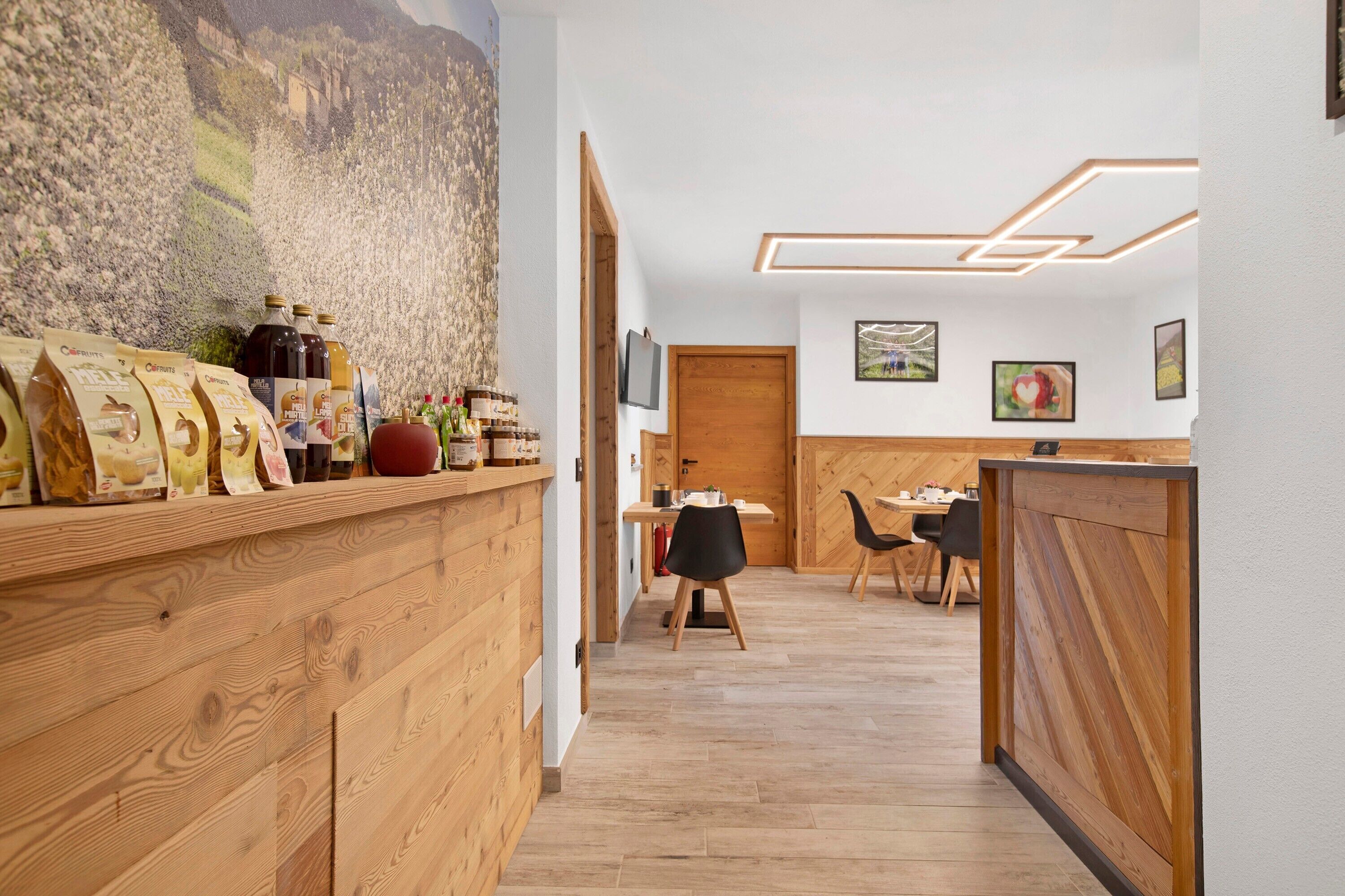 A wooden reception desk with a mountainous mural, a dining area with chairs and a table, and a wooden partition.