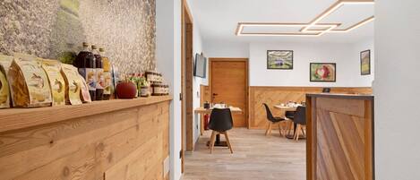 A wooden reception desk with a mountainous mural, a dining area with chairs and a table, and a wooden partition.