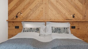 Un letto con biancheria bianca e due cuscini, soffitto in legno con motivo a V e due lampade fissate al muro.
