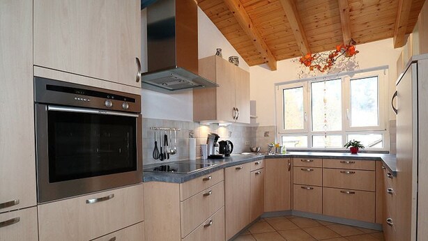 A modern kitchen with a built-in oven, stainless steel appliances, wooden cabinets, and a window with a view.