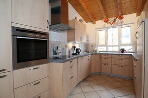A modern kitchen with a built-in oven, stainless steel appliances, wooden cabinets, and a window with a view.