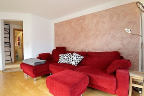 Ein rotes Sofa mit geometrischem Kissen, dazu ein passender Hocker und eine hohe Stehlampe.