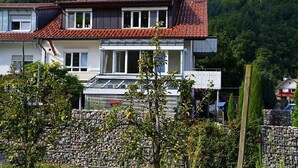 A two-story house with a red-tiled roof, solar panels, and a stone wall in the foreground.
