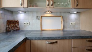 A kitchen with wooden cabinets, a marble countertop, and a glass-fronted upper cabinet.