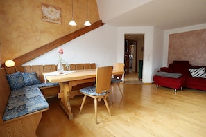 Ein gemütliches Wohnzimmer mit einem Holzesstisch, einem roten Sofa und einer eingebauten Bank mit Kissen.