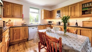 A kitchen with wooden cabinets, a dining table with chairs, and a window providing natural light. - Spacious Argyll Farmhouse in an Idyllic Setting (Dunoon)