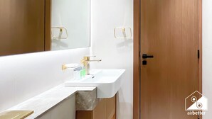 Un baño moderno con un lavamanos blanco, grifería dorada y un espejo grande.