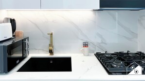 Una cocina moderna con un lavamanos negro, microondas integrado, estufa a gas y salpicadero de mármol.