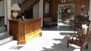 Un vaste espace de vie comprenant un comptoir d’accueil en bois, un escalier et un coin salon avec plusieurs chaises et un canapé.
