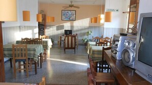 Un espace repas avec des tables et des chaises en bois, un ventilateur de plafond et un téléviseur.