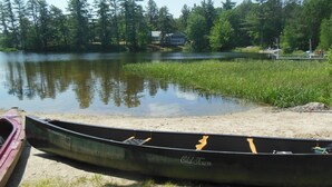 A canoe named "Old Town" on a sandy shore with a calm lake and trees in the background.