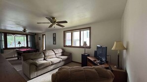 A living room with a sofa, a television, a pool table, and a ceiling fan.