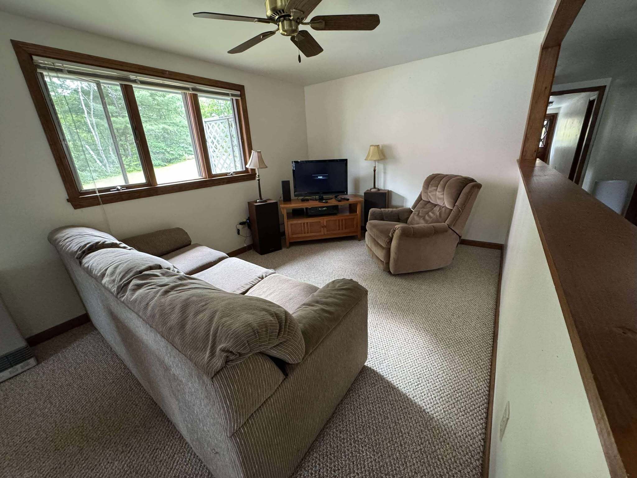 A living room with a sofa, a recliner, a TV on a wooden stand, and a ceiling fan.