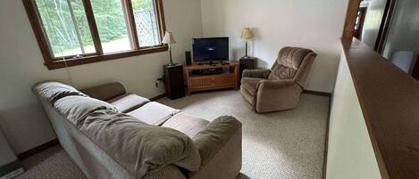 A living room with a sofa, a recliner, a TV on a wooden stand, and a ceiling fan.