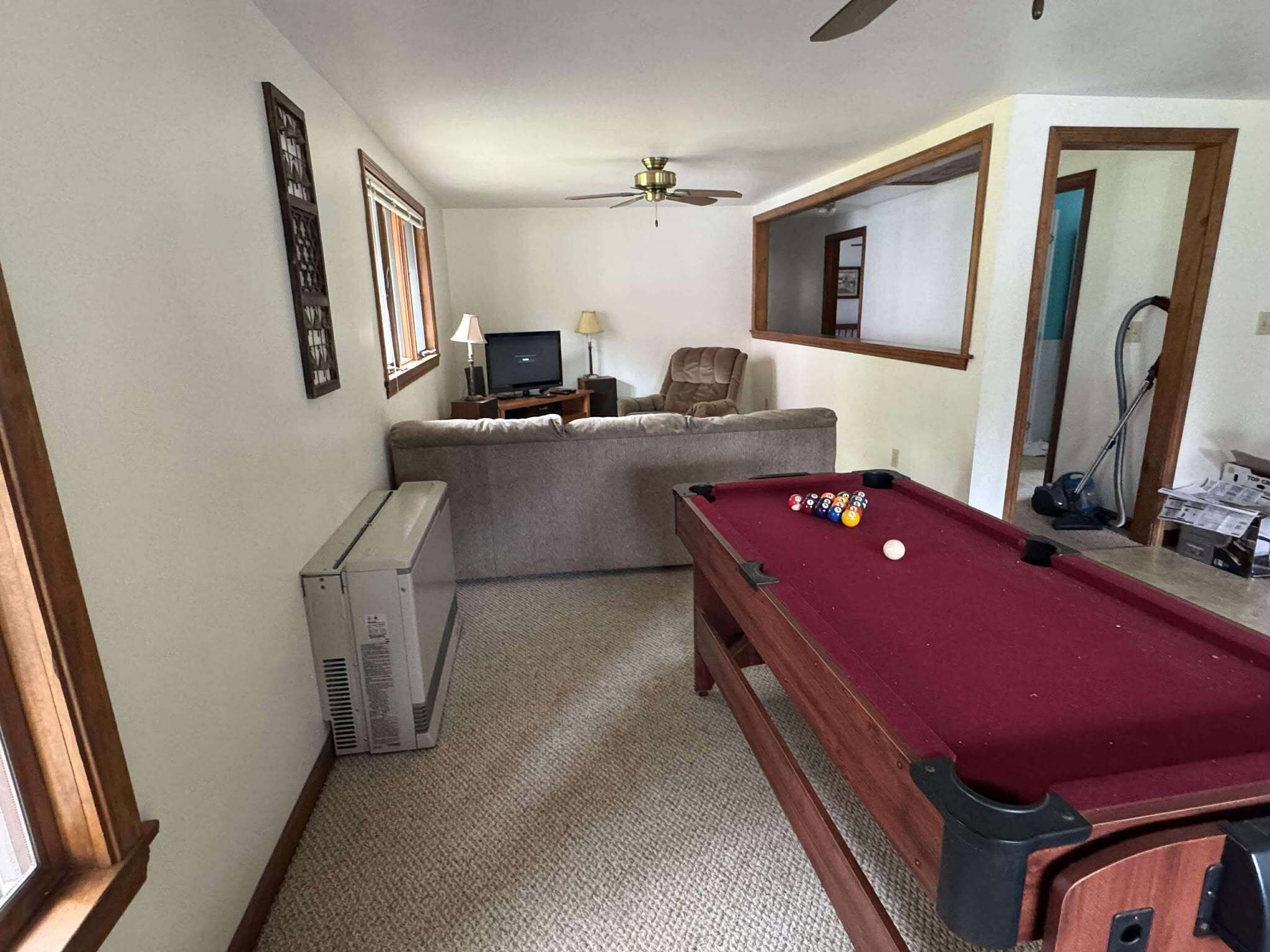 Una habitación con mesa de billar, televisor, sofá y ventilador de techo.