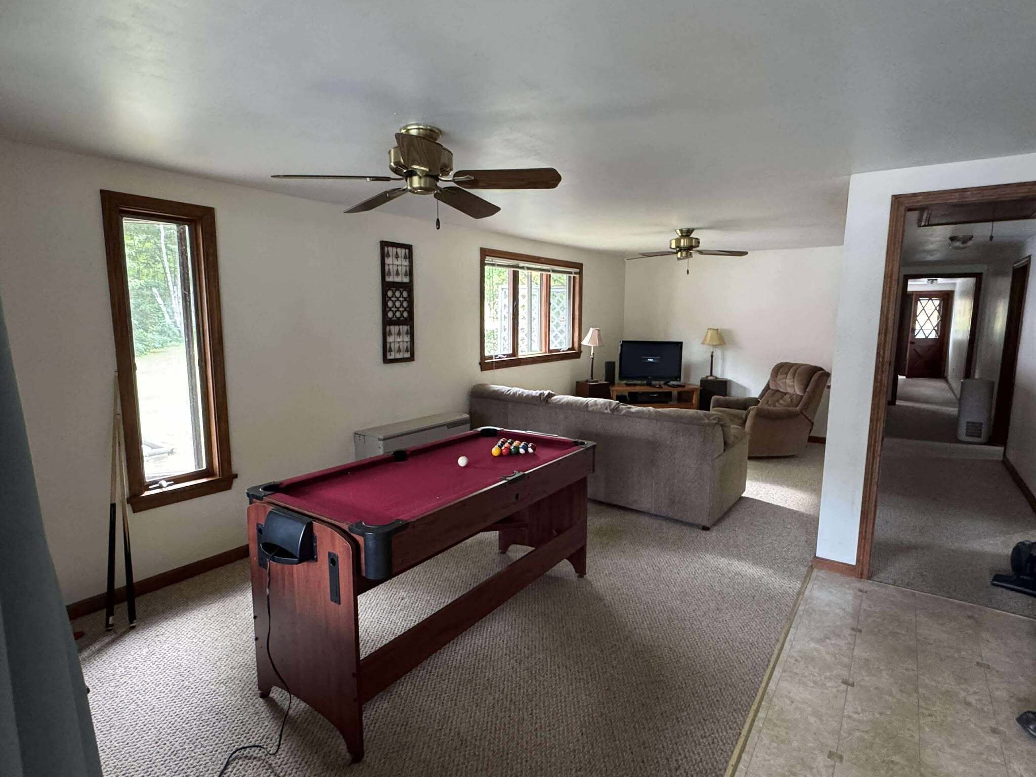 A living room with a pool table, two ceiling fans, a television, and a sofa.