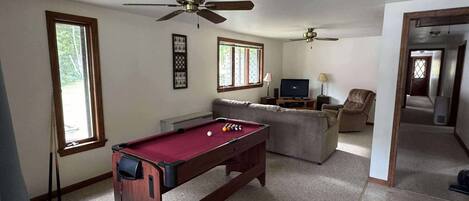 A living room with a pool table, two ceiling fans, a television, and a sofa.