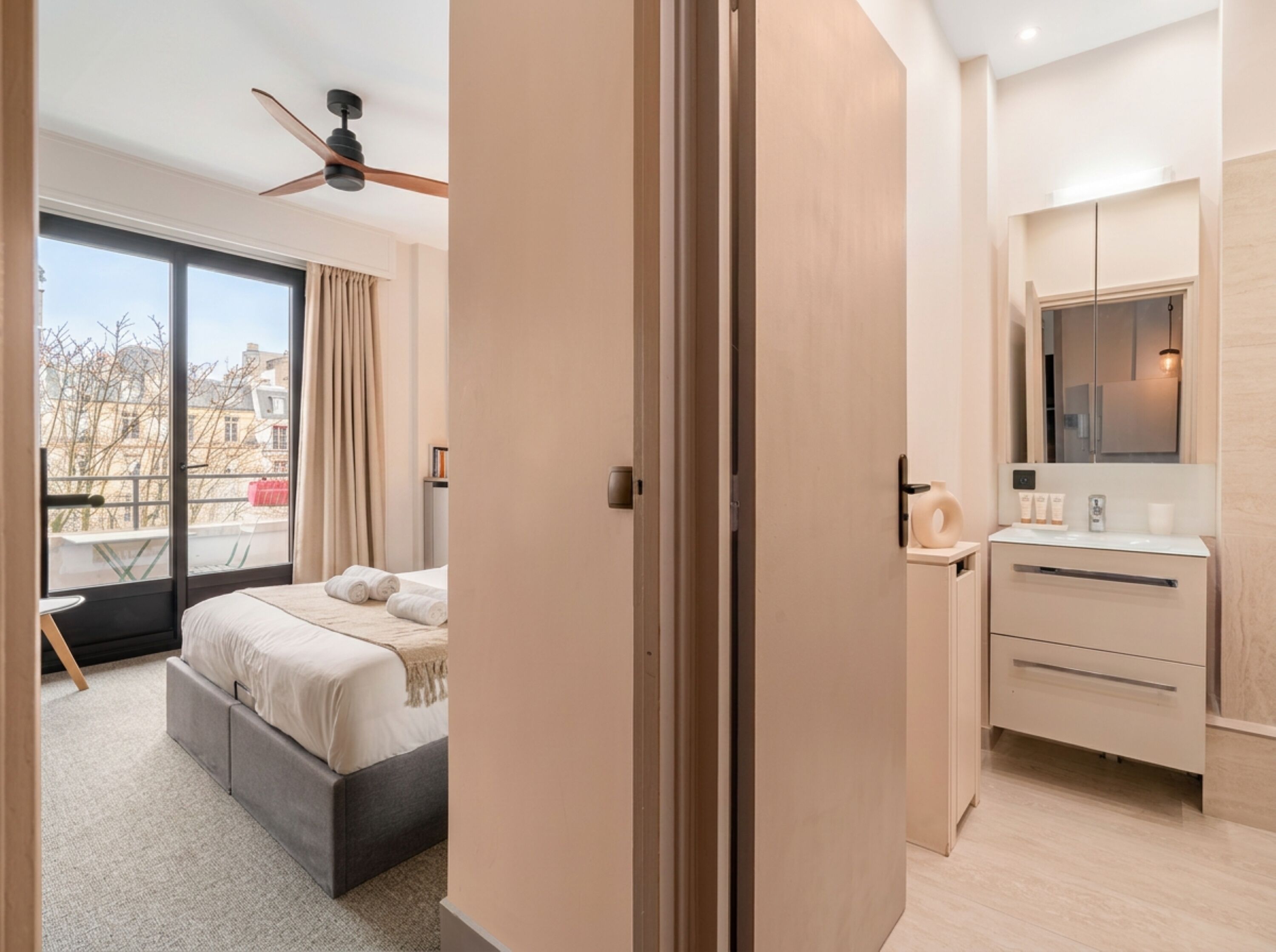 A modern hotel room with a bed, a desk, a mirror, and a view of the outside.