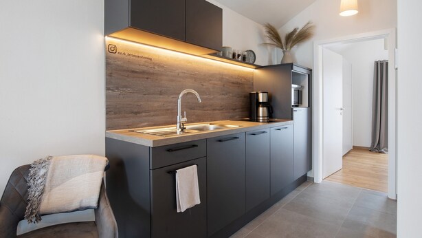 A modern kitchen with a built-in oven, a coffee machine, and a wooden backsplash.