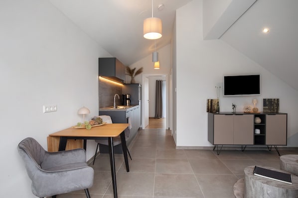Una cocina moderna con comedor, un televisor montado en la pared y una escalera que sube a otro nivel.