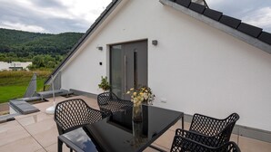 A modern outdoor patio with a glass table, black mesh chairs, and a vase with flowers.