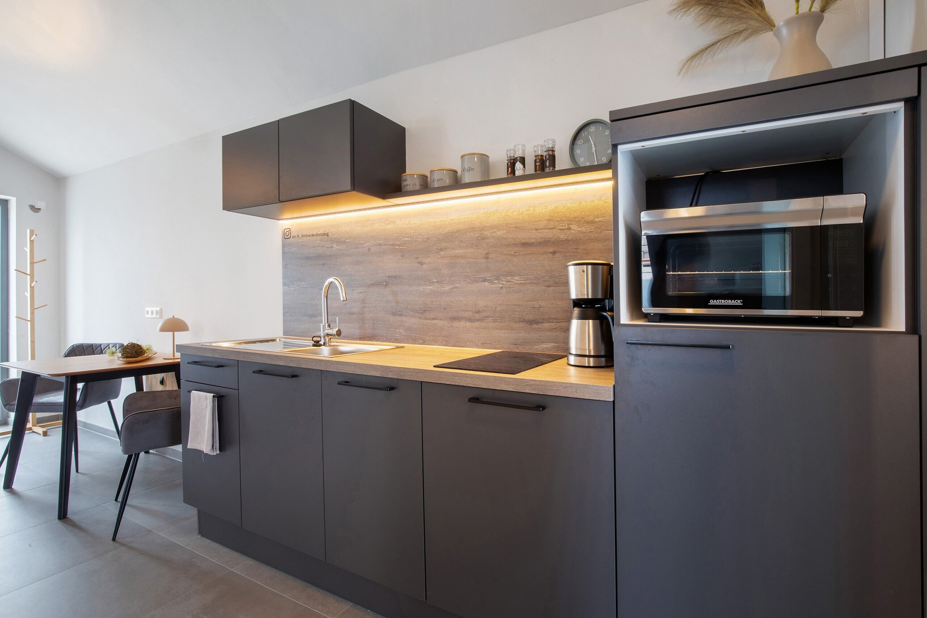 Een moderne keuken met een ingebouwde magnetron, een koffiezetapparaat en een houten spatwand.