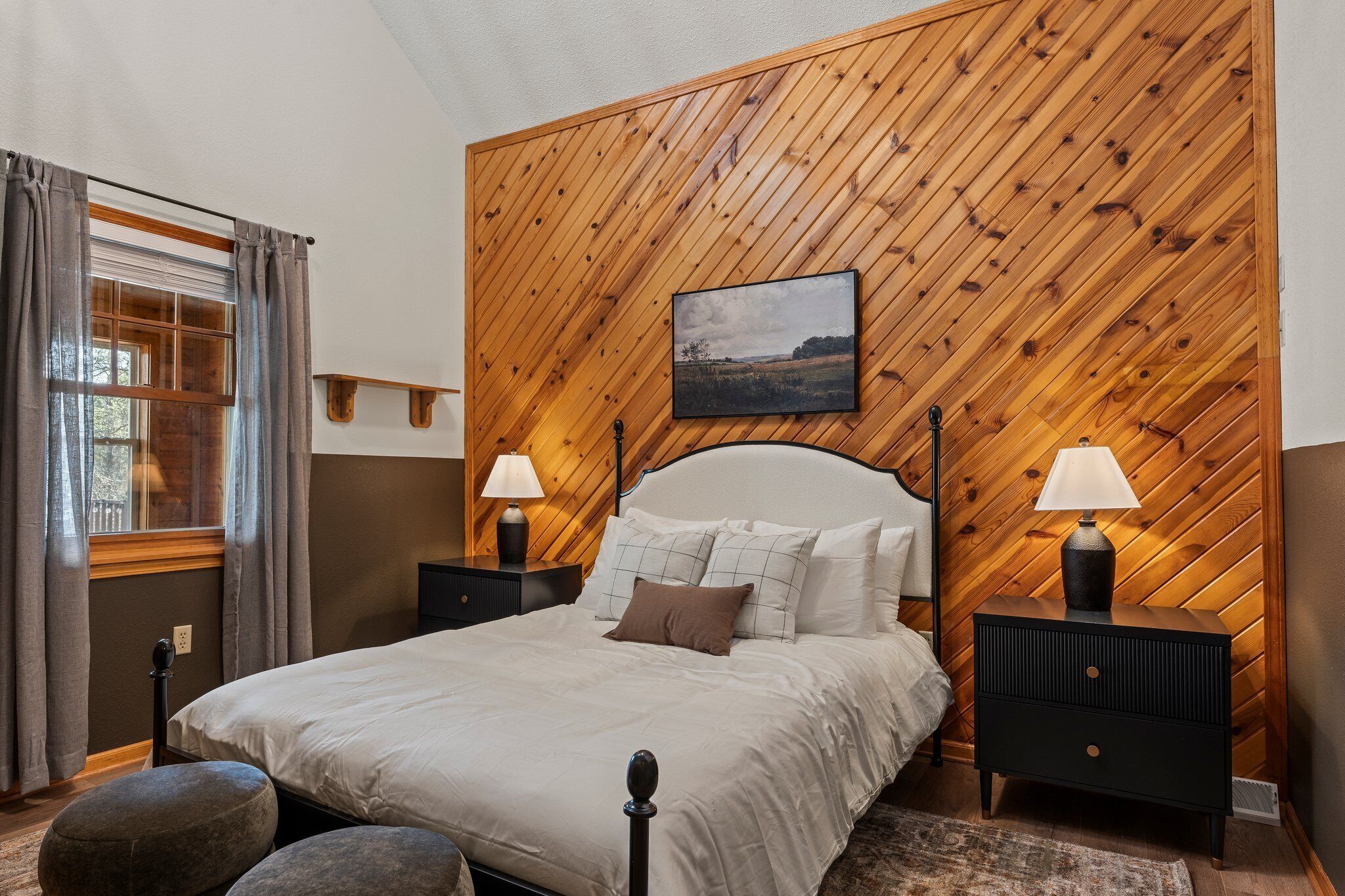 A bedroom with a wooden paneled headboard, a bed with white linens, two bedside tables with lamps, and a window with curtains.