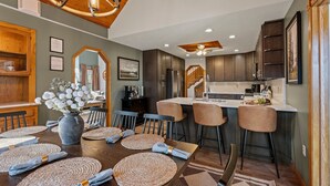 Een moderne keuken met donkere kastjes, een centraal eiland en een eethoek met een houten tafel en stoelen.