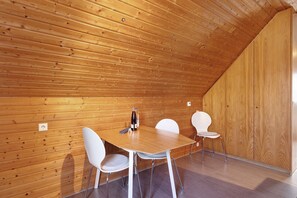 A room with a wooden sloped ceiling, a wooden wall, a wooden table with chairs, and a bottle on the table.