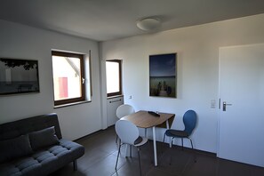 A modern room with a sofa, a table with chairs, a painting, and a door. - Apartment 'Kajüte Without Balcony' with Lake View, Shared Terrace and Wi-Fi (Moos)