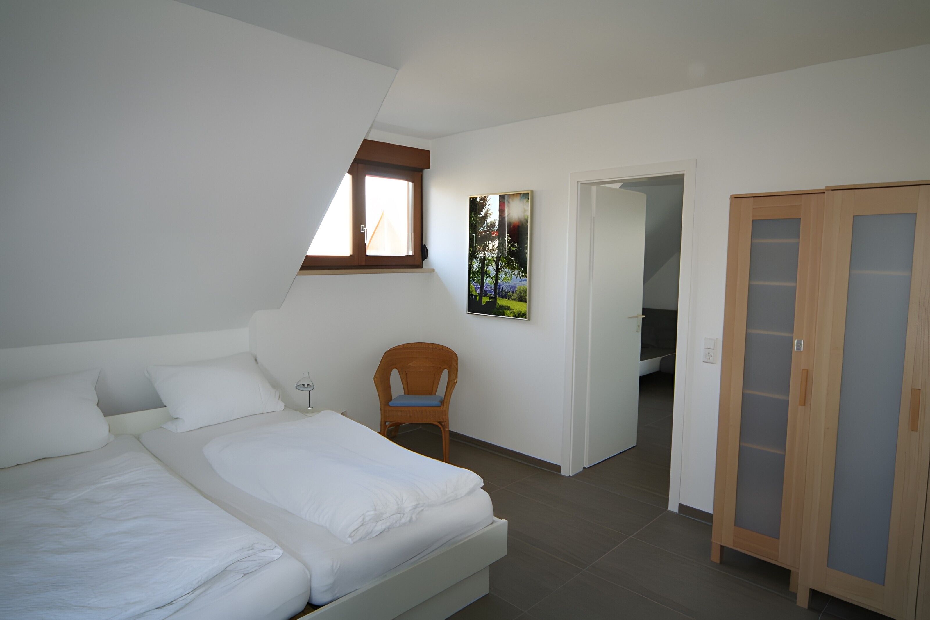 Ein Schlafzimmer mit Bett, Stuhl, Kleiderschrank und einer Tür zu einem anderen Raum.