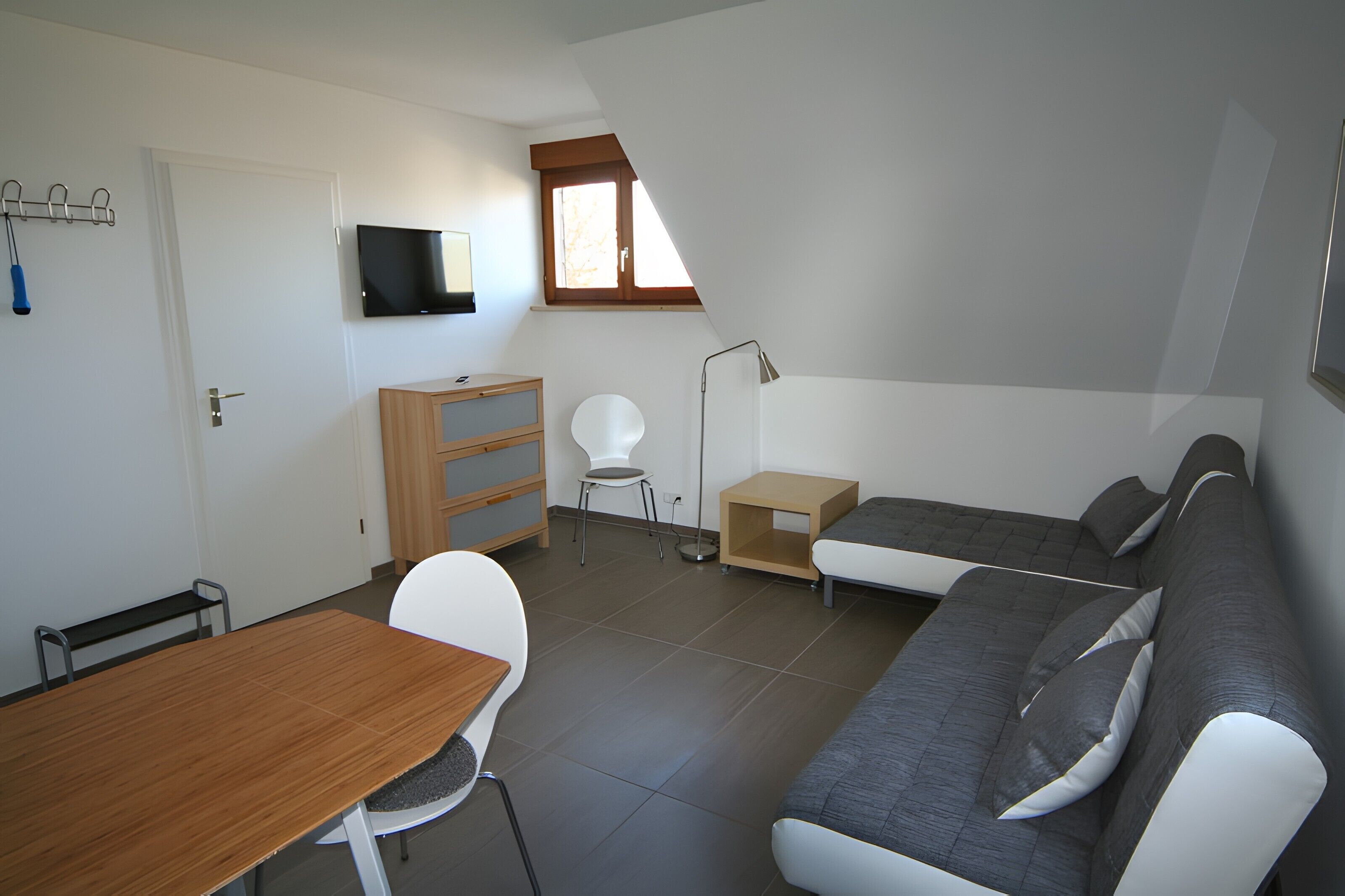 Ein gemütlicher Wohnbereich mit einer Couch, einem Esstisch, einem an der Wand befestigten Fernseher und einem kleinen Fenster.