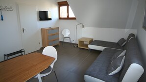 A compact living space with a sofa, a dining table, a TV mounted on the wall, and a small window. - Apartment 'Kajüte Without Balcony' with Lake View, Shared Terrace and Wi-Fi (Moos)