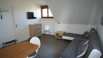 Ein gemütlicher Wohnbereich mit einer Couch, einem Esstisch, einem an der Wand befestigten Fernseher und einem kleinen Fenster.