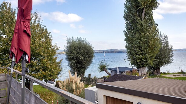 Une vue d’un lac avec un voilier, entouré d’arbres et d’un bâtiment doté d’un toit en métal.