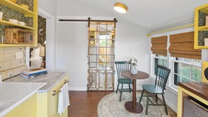 A kitchen with yellow shelves, a wooden door, a dining table with chairs, and a view through the door.