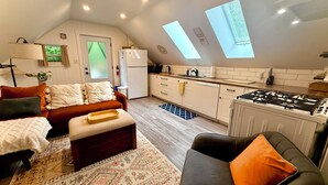 Een compact woongedeelte met een kitchenette, een bank, een eettafel en een vloerkleed met een patroon.