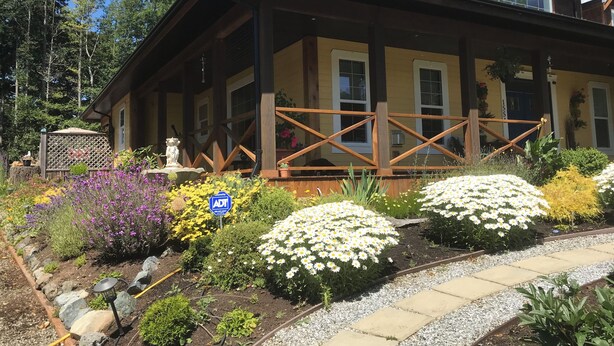 Een houten huis met een veranda, omringd door een tuin met diverse bloemen en een grindpad.