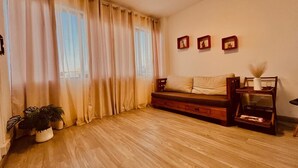 A room with wooden flooring, a sofa, a small table with a vase, and a potted plant.