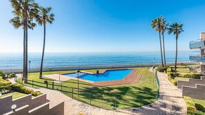 Piscina com vista para o oceano, rodeada por palmeiras e céu claro.
