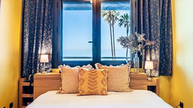 Cama com vista para palmeiras e o oceano pela janela.