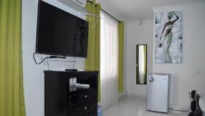 A room with a TV mounted on the wall, a black cabinet with drawers, a white refrigerator, and a painting on the wall. - Posada Cocos Place (San Andrés)