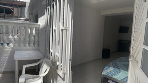 A small, sunlit room with a white table and chair, a bed with patterned bedding, and a balcony with a white railing. - Posada Cocos Place (San Andrés)