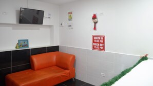 A waiting area with a red sofa, a mounted TV, and a 'Check In' sign. - Posada Cocos Place (San Andrés)