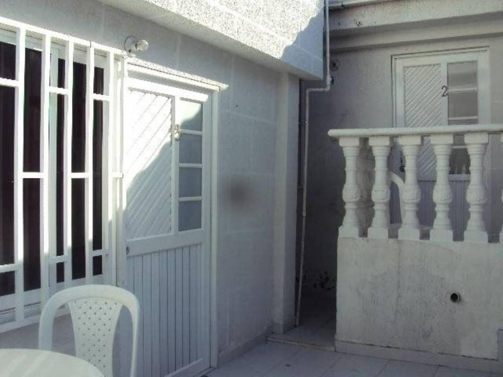 A white balcony with a balustrade, a white door with a window, and a white chair.