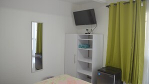 A bedroom with a bed, a TV mounted on the wall, a wardrobe, and a desk with a computer. - Posada Cocos Place (San Andrés)