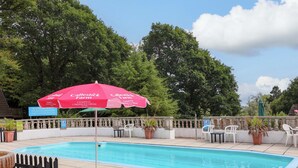 Un espace piscine agrémenté d’un parasol rouge, de chaises longues et d’un panneau indiquant la ferme de Callestick.