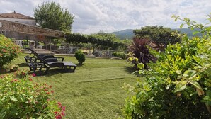 Un césped cuidado con muebles de exterior, un muro de piedra y abundante vegetación.