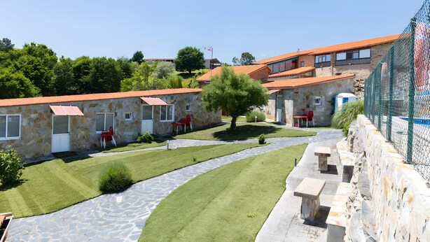 Un edificio de piedra con techo rojo, un camino empedrado y un área cercada con piscina.